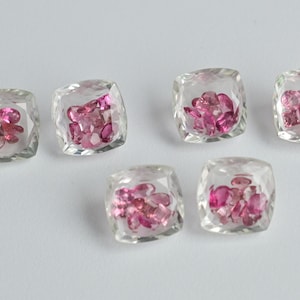 May include: Six clear square-shaped gemstone settings with pink gemstones inside.