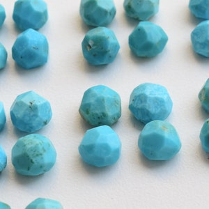 Puede incluir: Primer plano de cuentas de piedras preciosas de turquesa facetadas. Cada cuenta es de un color azul claro vibrante con un dise&ntilde;o geom&eacute;trico multifac&eacute;tico. Las cuentas est&aacute;n dispuestas juntas, mostrando sus superficies pulidas.