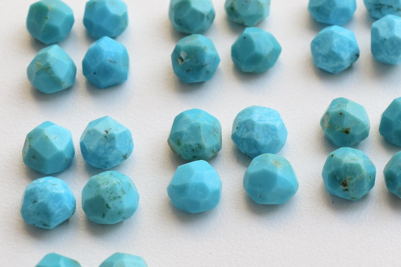 Puede incluir: Primer plano de cuentas de piedras preciosas de turquesa facetadas. Cada cuenta es de un color azul claro vibrante con un dise&ntilde;o geom&eacute;trico multifac&eacute;tico. Las cuentas est&aacute;n dispuestas juntas, mostrando sus superficies pulidas.