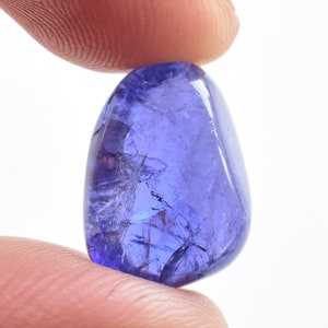 K&ouml;nnte beinhalten: Ein polierter, oval geformter Tansanit-Edelstein, der zwischen zwei Fingern gehalten wird. Der Edelstein hat eine tiefviolett-blaue Farbe mit sichtbaren inneren Br&uuml;chen. Der Hintergrund ist schlicht wei&szlig; und hebt die Farbe und Klarheit des Steins hervor.