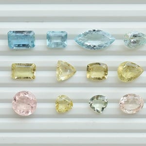 May include: A collection of gemstones in different shapes and colours, including blue, yellow, and pink. The gemstones are displayed on a white surface, highlighting their various cuts and clarity. Suitable for jewellery making.
