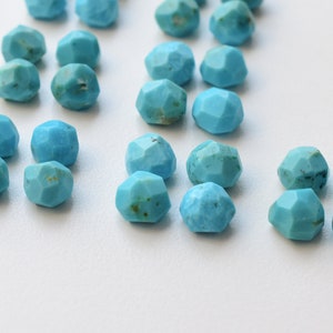 Puede incluir: Una colecci&oacute;n de cuentas de piedra turquesa, cada una con una forma facetada irregular. Las cuentas son de un color azul vibrante y est&aacute;n dispersas sobre una superficie blanca.
