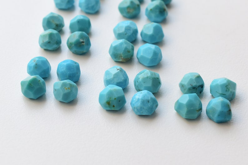 Puede incluir: Una colecci&oacute;n de cuentas de piedra turquesa, cada una con una forma facetada irregular. Las cuentas son de un color azul vibrante y est&aacute;n dispersas sobre una superficie blanca.
