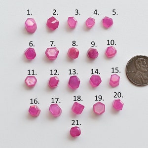 May include: Twenty-one pink faceted gemstones arranged in rows on a white surface. A US penny is included for scale.