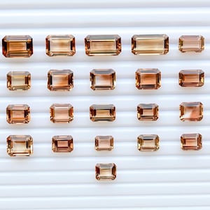 May include: A collection of rectangular-cut gemstones in shades of amber. The gems are arranged on a white, ridged surface. The gemstones vary in size and have a gradient effect. Ideal for jewellery making, the gems are in various sizes.
