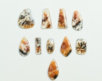 May include: A collection of polished gemstones in various shapes, including oval, teardrop, and rectangular. The stones feature a mix of colors, with dominant shades of orange, brown, black, and white, creating unique patterns. These gemstones are ideal for jewelry making.