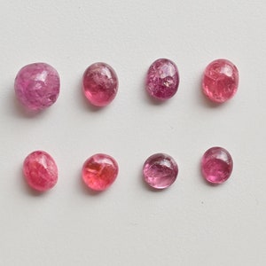 K&ouml;nnte beinhalten: Acht rosa, oval geformte Edelsteine mit einer glatten, polierten Oberfl&auml;che. Die Edelsteine sind in zwei Reihen zu je vier angeordnet, wobei die obere Reihe leicht versetzt zur unteren Reihe ist.