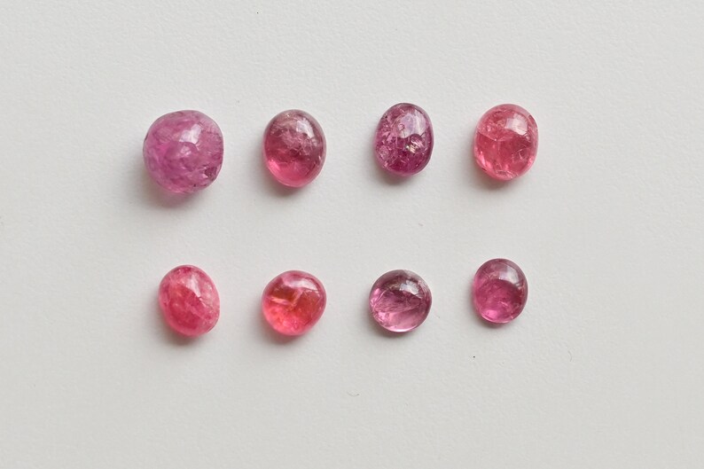 K&ouml;nnte beinhalten: Acht rosa, oval geformte Edelsteine mit einer glatten, polierten Oberfl&auml;che. Die Edelsteine sind in zwei Reihen zu je vier angeordnet, wobei die obere Reihe leicht versetzt zur unteren Reihe ist.