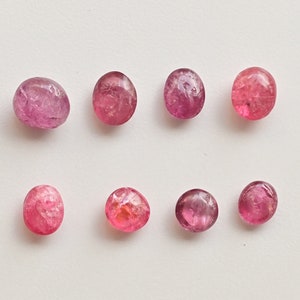 K&ouml;nnte beinhalten: Acht ovale Edelsteine in Rosa und Rot mit einer rauen, strukturierten Oberfl&auml;che.