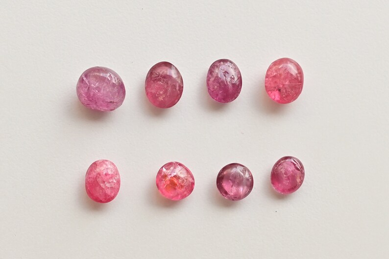 K&ouml;nnte beinhalten: Acht ovale Edelsteine in Rosa und Rot mit einer rauen, strukturierten Oberfl&auml;che.