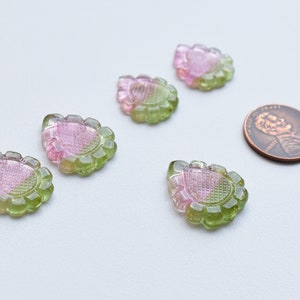 May include: Five pink and green teardrop-shaped glass beads with a decorative pattern. The beads are arranged in a semi-circle on a white surface.