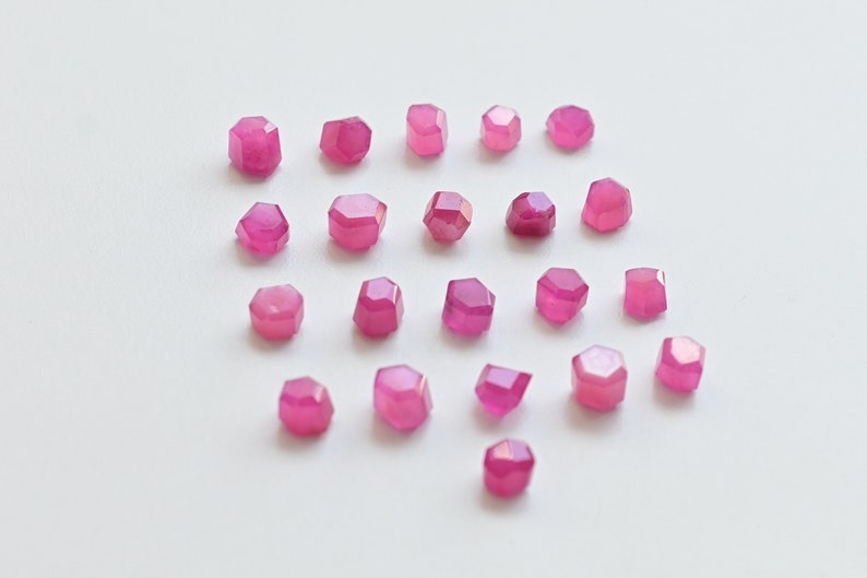 May include: A collection of 20 pink faceted gemstone beads. The beads are arranged in a heart shape on a white background.