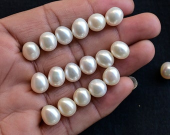 May include: A collection of white oval-shaped pearls, some arranged in rows and one pearl sitting alone on a dark surface.