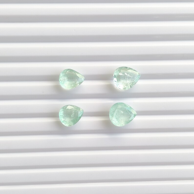 Puede incluir: Cuatro gemas facetadas en forma de l&aacute;grima, de color verde p&aacute;lido y de diferentes tama&ntilde;os. Las gemas son transl&uacute;cidas y est&aacute;n dispuestas en un patr&oacute;n cuadrado sobre una superficie blanca estriada. Ideales para la fabricaci&oacute;n de joyas.