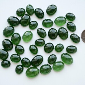 May include: A collection of oval, dark green glass stones on a white surface. A penny is included for size comparison. The stones vary in shade from light to dark green and have a glossy finish. These could be used for crafts or decorative purposes.