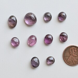 May include: Ten purple and pink oval-shaped gemstones of various sizes, with a penny for scale.