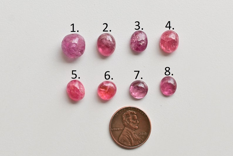 K&ouml;nnte beinhalten: Acht rosa Turmalin-Edelsteine, nummeriert von 1 bis 8, sind in zwei Reihen zu je vier angeordnet. Ein US-Cent ist zur Gr&ouml;&szlig;enbestimmung enthalten.