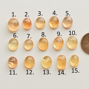 May include: Fifteen yellow-orange oval-shaped gemstones, numbered 1 through 15, are arranged in three rows. A U.S. penny is included for size comparison.