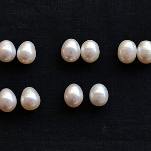 Puede incluir: Seis pares de perlas ovaladas blancas sobre un fondo de tela negro.