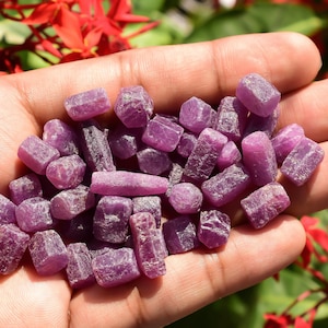 Może przedstawiać: Kolekcja małych, surowych, fioletowych kryształów rubinu. Kryształy mają różne kształty i rozmiary i mają naturalny, nieoszlifowany wygląd.