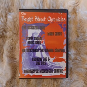May include: A DVD case for "The Haight Street Chronicles Vol. 1" featuring a vibrant orange and purple design. The cover lists bands like The Grateful Dead, Moby Grape, and Steve Miller Blues Band. The case is black.