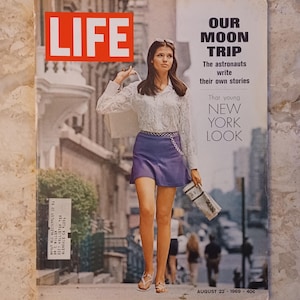 May include: A vintage LIFE magazine cover from August 22, 1969, featuring a woman in a white lace top and purple skirt. The cover text reads "OUR MOON TRIP" and "NEW YORK LOOK". The woman is walking on a city street.