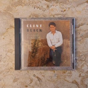 May include: A CD case featuring the album "Killin' Time" by Clint Black. The cover art shows a man in a white shirt and jeans leaning against a rock wall. The artist's name is printed in large, bold letters.