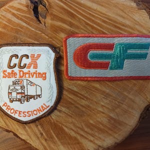 May include: Two embroidered patches. One is shield-shaped with the text "CCX Safe Driving Professional" and a truck graphic. The other is rectangular with "CF" in red and teal on a gray background, outlined in red.