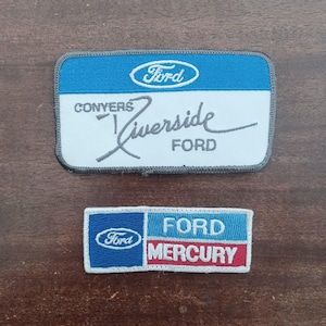 May include: Two vintage Ford patches. The larger patch has a blue top section with the Ford logo, white center with "CONVERS Riverside FORD" text. The smaller patch has a blue section with the Ford logo, and text "FORD MERCURY" in blue and red.