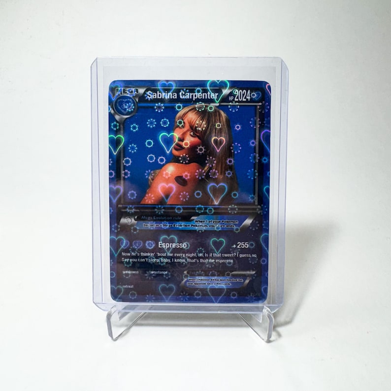 Op de afbeelding: Een blauwe en witte Pok&eacute;mon-kaart met een holografische afbeelding van Sabrina Carpenter. De kaart heeft een blauwe achtergrond met witte harten en cirkels. De tekst op de kaart luidt "Sabrina Carpenter 2024" en "Espresso".