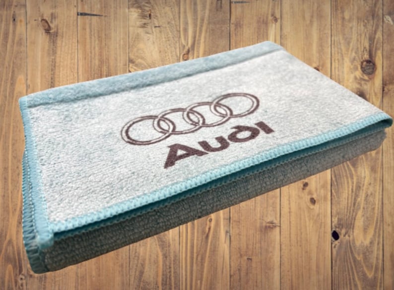 May include: A light blue microfiber cleaning cloth with the Audi logo and the word "Audi" printed in brown.