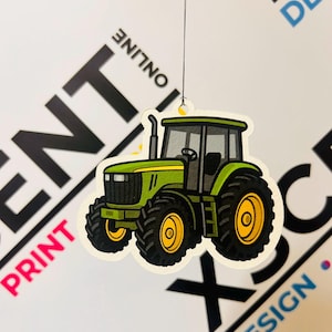 May include: A green and yellow tractor-shaped ornament with black tires and a gray cab. The ornament is suspended by a thin string. The background includes the words "PRINT ONLINE" and "DESIGN".