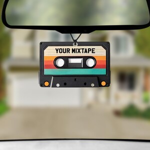 May include: A retro-style car air freshener shaped like a cassette tape with the text "YOUR MIXTAPE" printed on it. The cassette is brown, orange, yellow, green, and black.