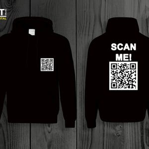 Op de afbeelding: Zwarte hoodie met een witte QR-code en de tekst "SCAN ME!" gedrukt op de achterkant.