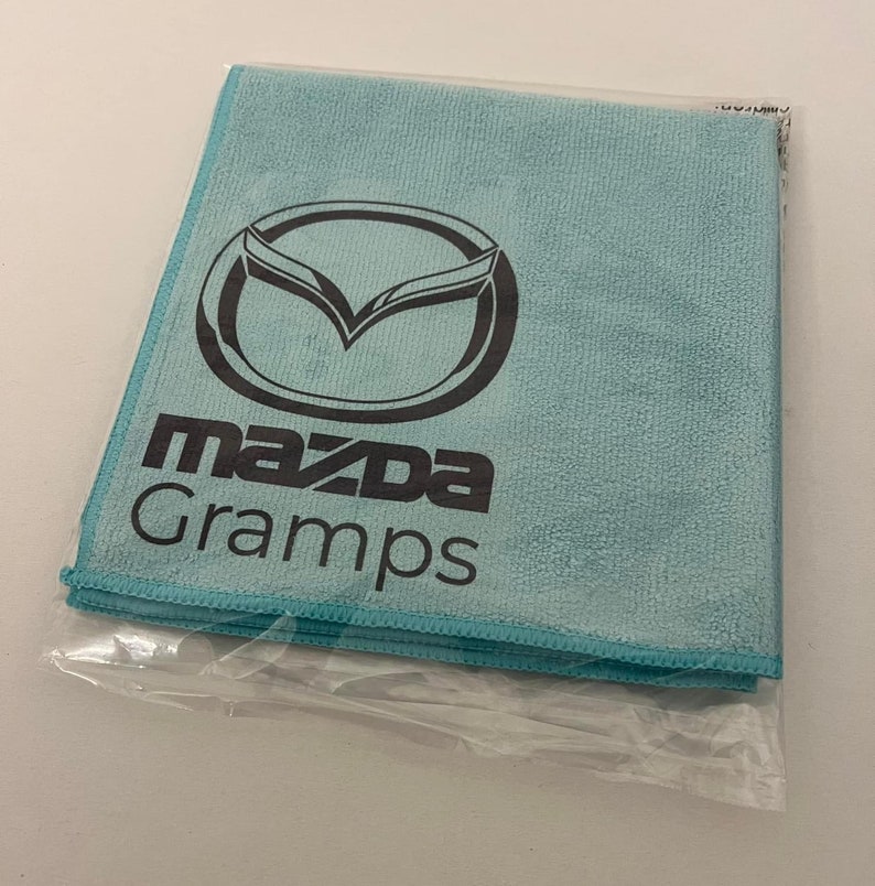 May include: A light blue microfiber cleaning cloth with the Mazda logo and the word "Gramps" printed in black.