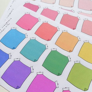 Pode incluir: Uma folha de adesivos quadrados coloridos com cantos arredondados. Cada adesivo tem uma borda branca e um contorno preto. Os adesivos estão dispostos em linhas e colunas sobre um fundo branco.