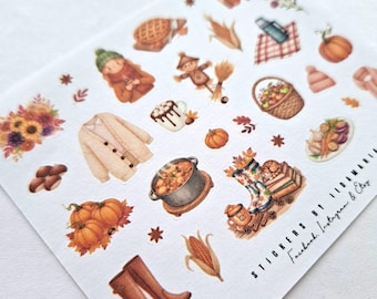 May include: A sheet of autumn-themed stickers featuring illustrations of pumpkins, boots, a scarecrow, a pot of stew, and a cozy sweater. Other images include a basket of apples, a mug of hot chocolate, and fall foliage. The stickers are in warm, earthy tones.