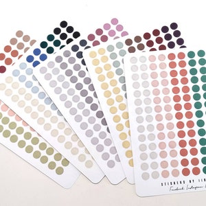 May include: Seven sheets of sticker dots in various colors, including beige, light blue, gray, yellow, light pink, red, green, and dark green. Each sheet has 49 dots arranged in a grid pattern. The sheets are fanned out and the bottom sheet has the text "Stickers by Vivamaria Facebook Instagram & Etsy".