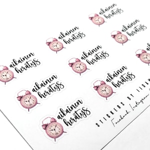 Puede incluir: Un conjunto de ocho pegatinas de reloj despertador rosa con el texto "aikainen herätys" en escritura negra. Las pegatinas están sobre un fondo blanco. El texto se traduce como "despertar oportuno" en inglés.