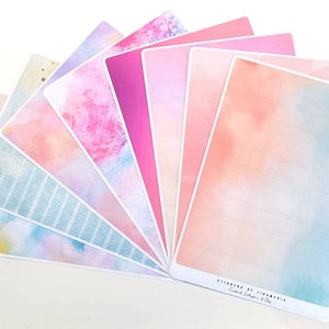 Könnte beinhalten: Ein Set mit acht pastellfarbenen Aquarell-Planer-Stickern mit verschiedenen Designs, darunter ein geometrisches Muster, ein rosa-blauer Farbverlauf und ein einfarbiges Rosa. Die Sticker sind mit "Stickers by Strawberry", "Funktionale Sticker & Clips" beschriftet.