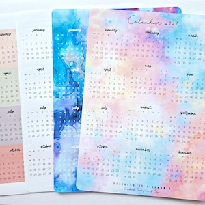 Könnte beinhalten: Ein Set aus vier rechteckigen Kalenderblättern für 2021 mit aquarellartigen Hintergründen in pastellfarbenen Rosa-, Blau- und Violettverläufen. Jedes Blatt zeigt zwölf Monate mit schwarzem Text, inklusive der Überschrift Calendar 2021.