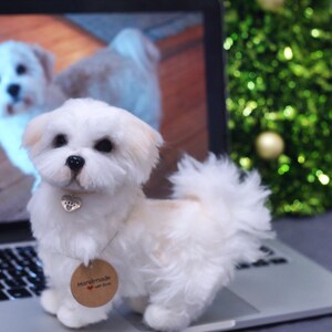 May include: A white and tan handmade felt dog toy, sitting on a laptop computer. The toy has a small silver heart charm around its neck and a brown tag that says "Handmade with love".