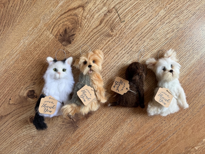 May include: Four plush animal ornaments: a white cat with black markings, two dogs in shades of brown and tan, and a white dog. Each has a small tag that says "Thank You".