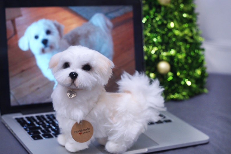 May include: A white and tan handmade felt dog toy, sitting on a laptop computer. The toy has a small silver heart charm around its neck and a brown tag that says "Handmade with love".