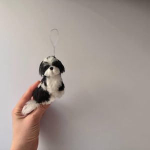 May include: A black and white Shih Tzu dog ornament with a loop for hanging. The small dog figurine is made of soft material and has a fluffy tail. The dog is sitting upright and has a sweet expression.