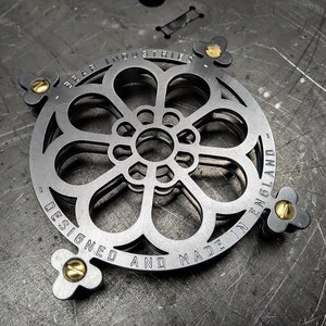 Könnte beinhalten: Ein Metalluntersetzer mit einem floralen Design. Der Untersetzer ist mit dem Text "Bear Industries Designed and Made in England" graviert.