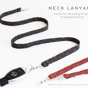 May include: Two fabric neck lanyards with a geometric pattern. One lanyard is black with gold accents and the other is red with gold accents. The lanyards are attached to a silver key chain with a car key.