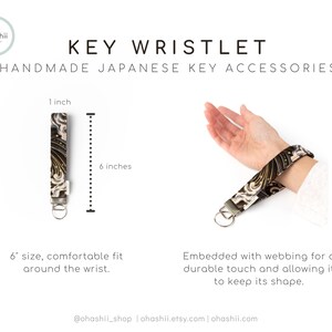 May include: A black and gold key wristlet with a Japanese-inspired pattern. The wristlet is 6 inches long and 1 inch wide. It is made with webbing for a durable touch and to keep its shape.