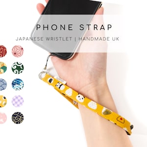 Puede incluir: Una correa de teléfono amarilla con un patrón de panda y bola de arroz. La correa está unida a una funda de teléfono negra. El texto "PHONE STRAP" y "JAPANESE WRISTLET | HANDMADE UK" se muestra sobre la funda del teléfono.