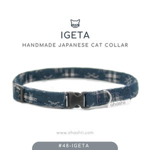 May include: A handmade Japanese cat collar with a blue and white patterned fabric. The collar has a black plastic buckle and a small white tag that reads "ohashii". The brand name "IGETA" is displayed above the collar.